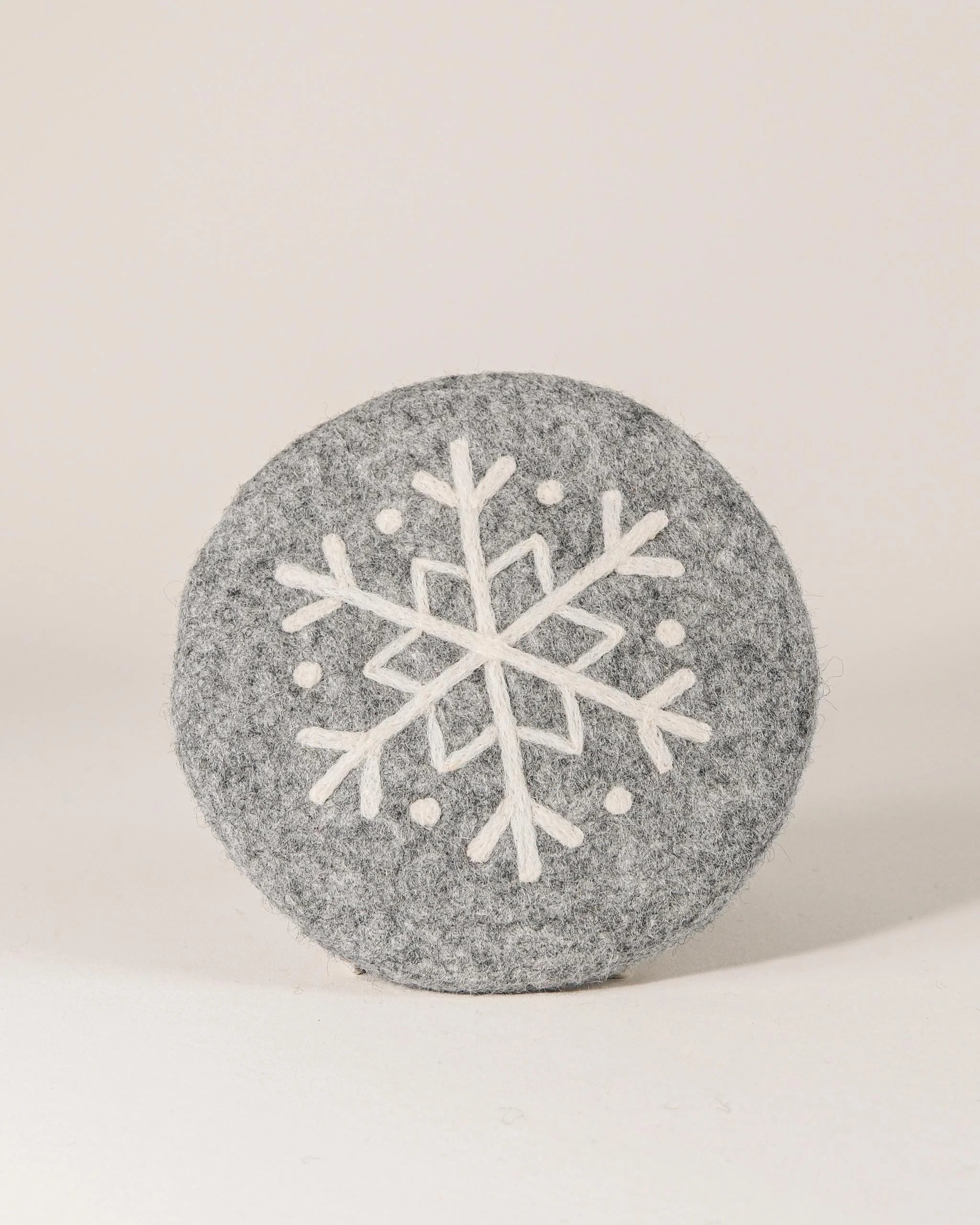 Dessous de plat boule en feutrine motif flocon sur un fond blanc.