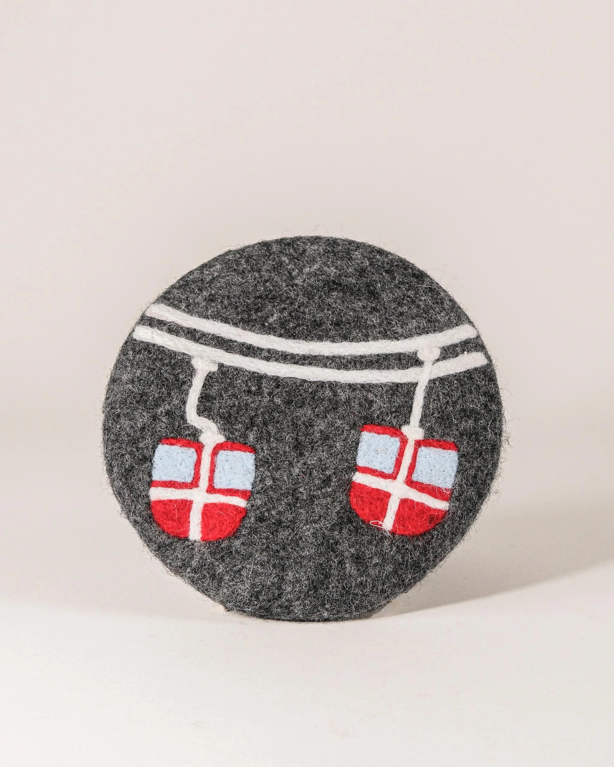 Dessous de plat boule en feutrine motif télécabine sur un fond blanc.