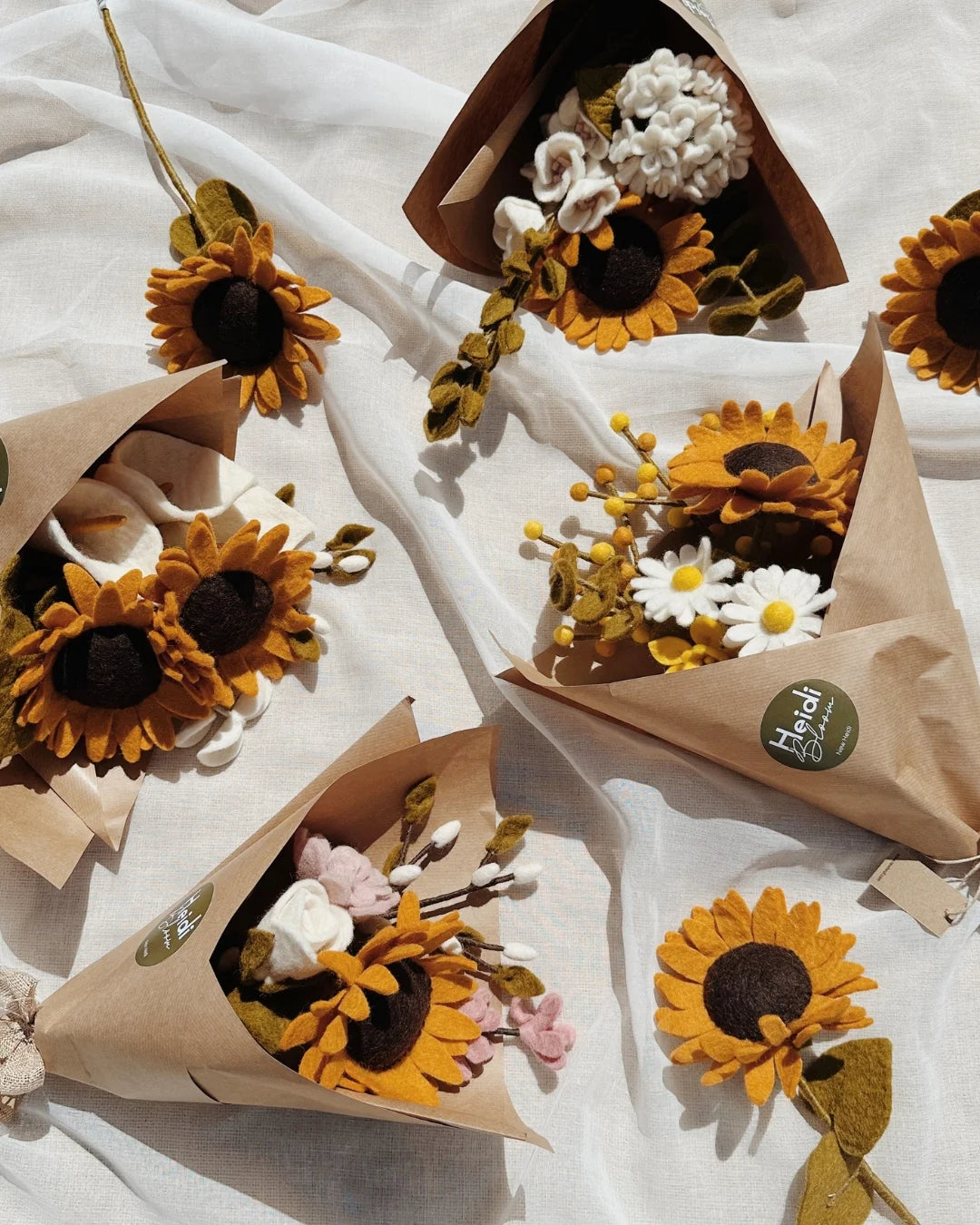 Plusieurs bouquet de fleurs en feutrine avec des tournesols posés sur un drap blanc
