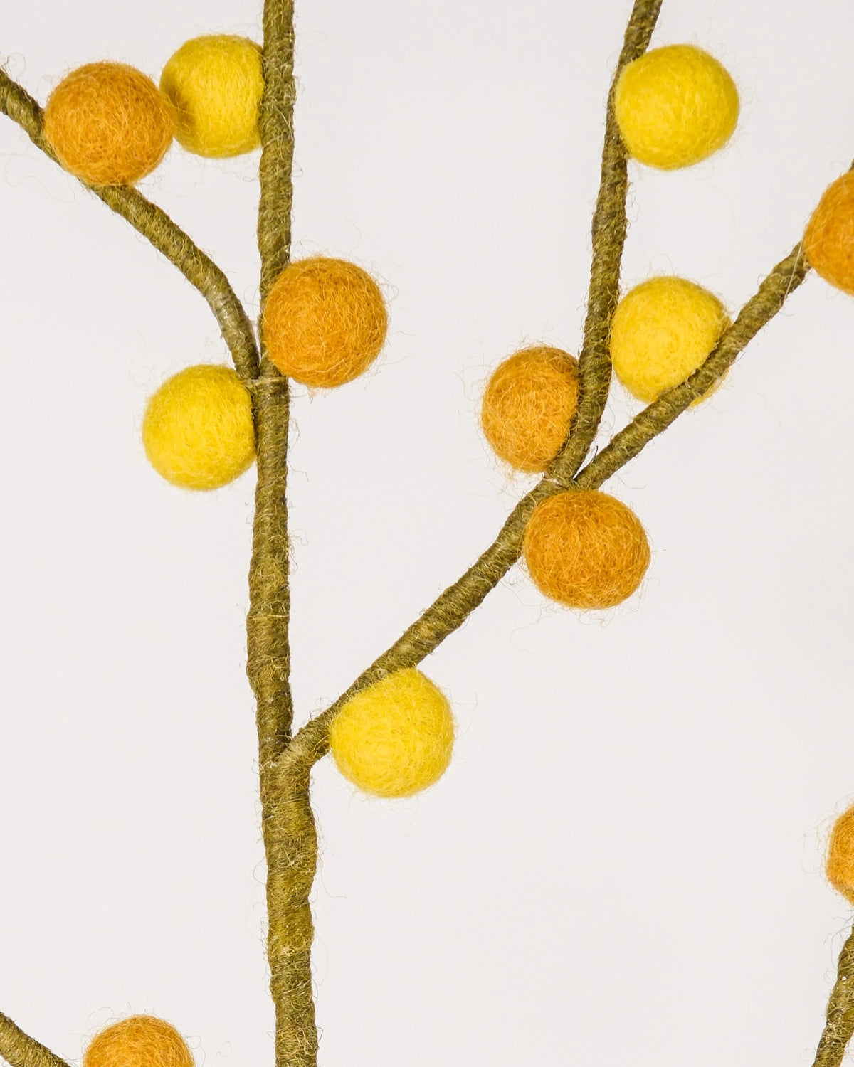 Photo zoom d'une branche de baies jaunes et oranges en feutrine sur un fond blanc style photo packshot.