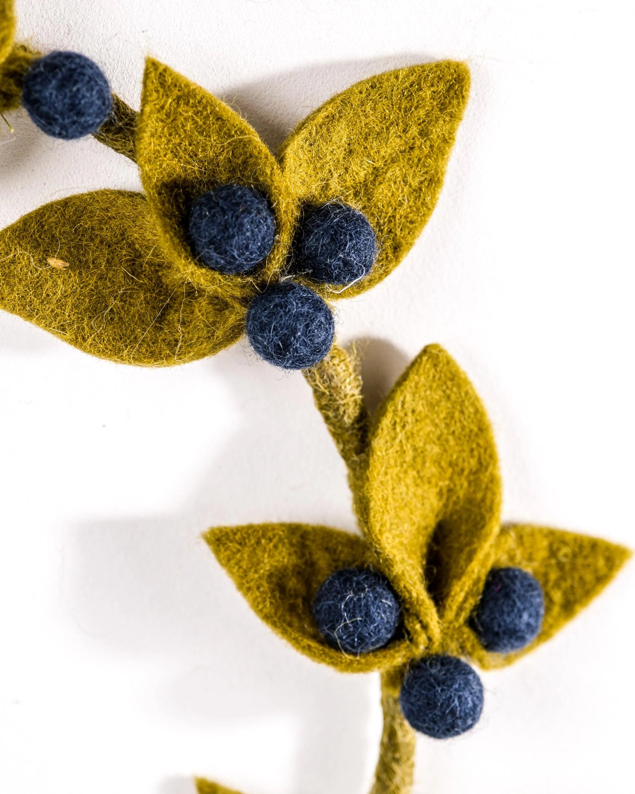 Couronne en feutrine myrtille sur un mur blanc detail zoom.