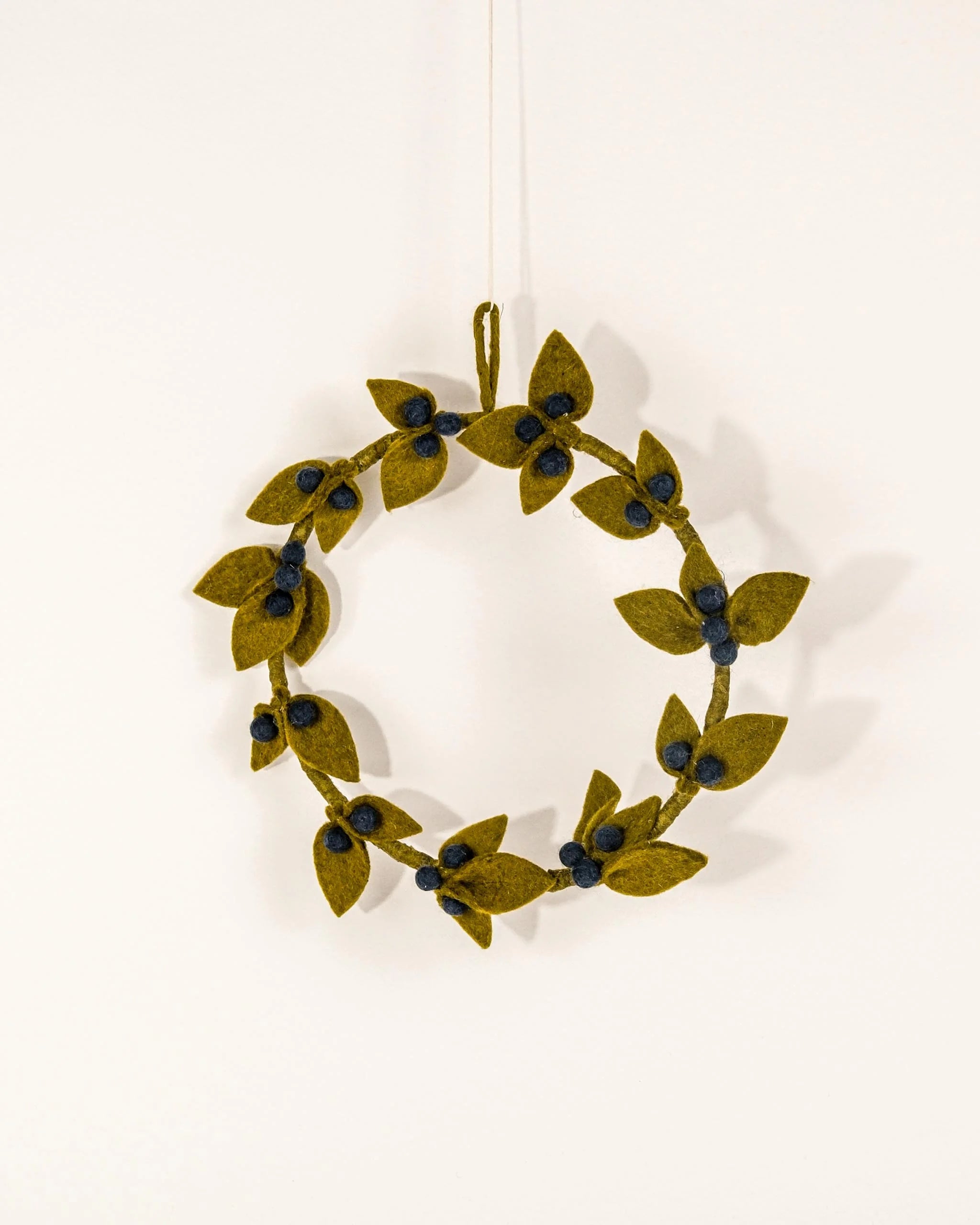 Couronne en feutrine myrtille sur un mur blanc.