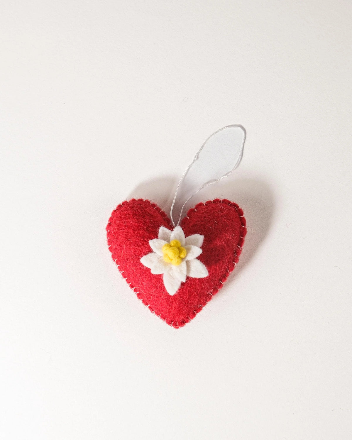 Coeur rouge a suspendre avec edelweiss sur fond blanc.