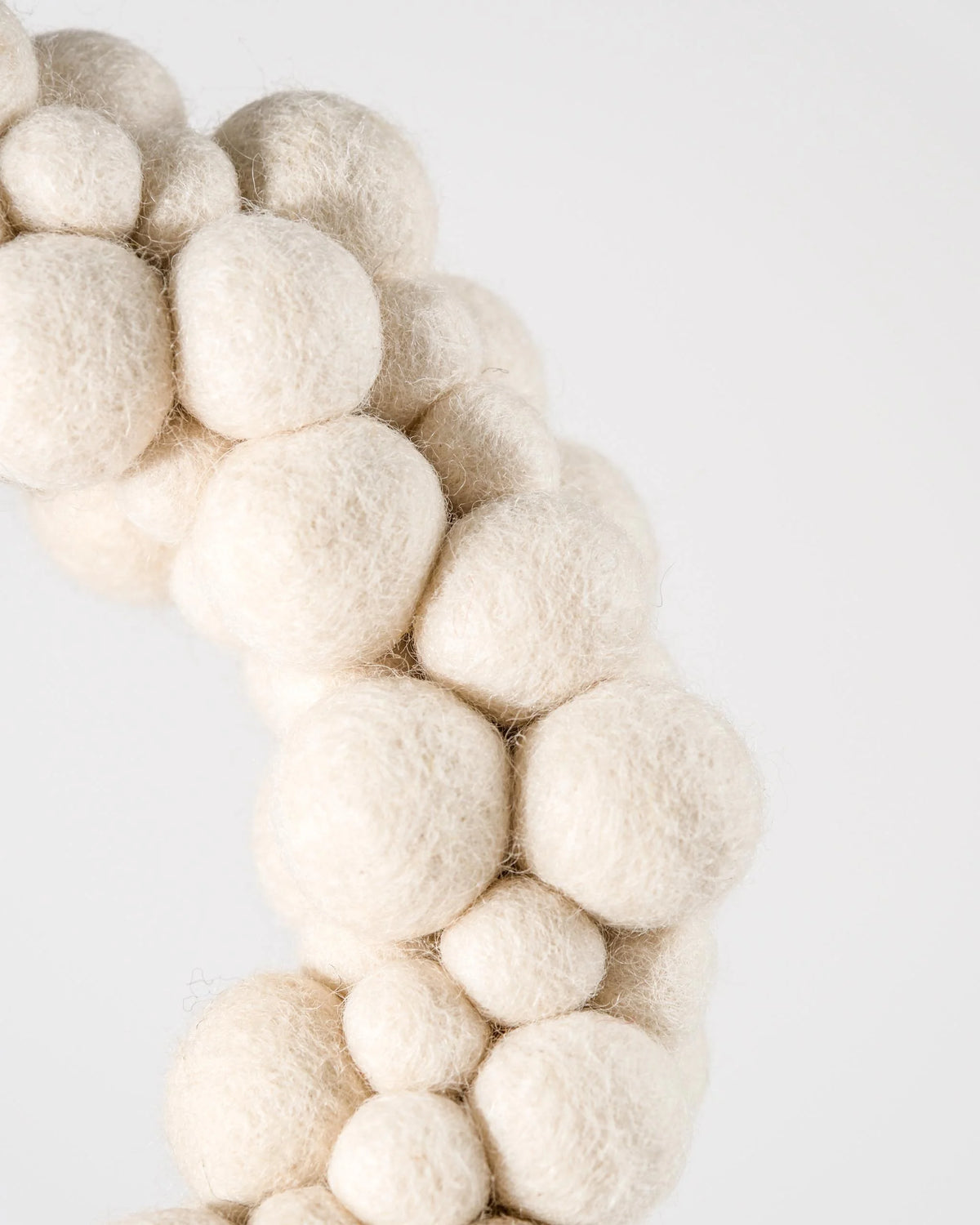 Couronne en feutrine boules blanche sur un mur blanc detail zoom.