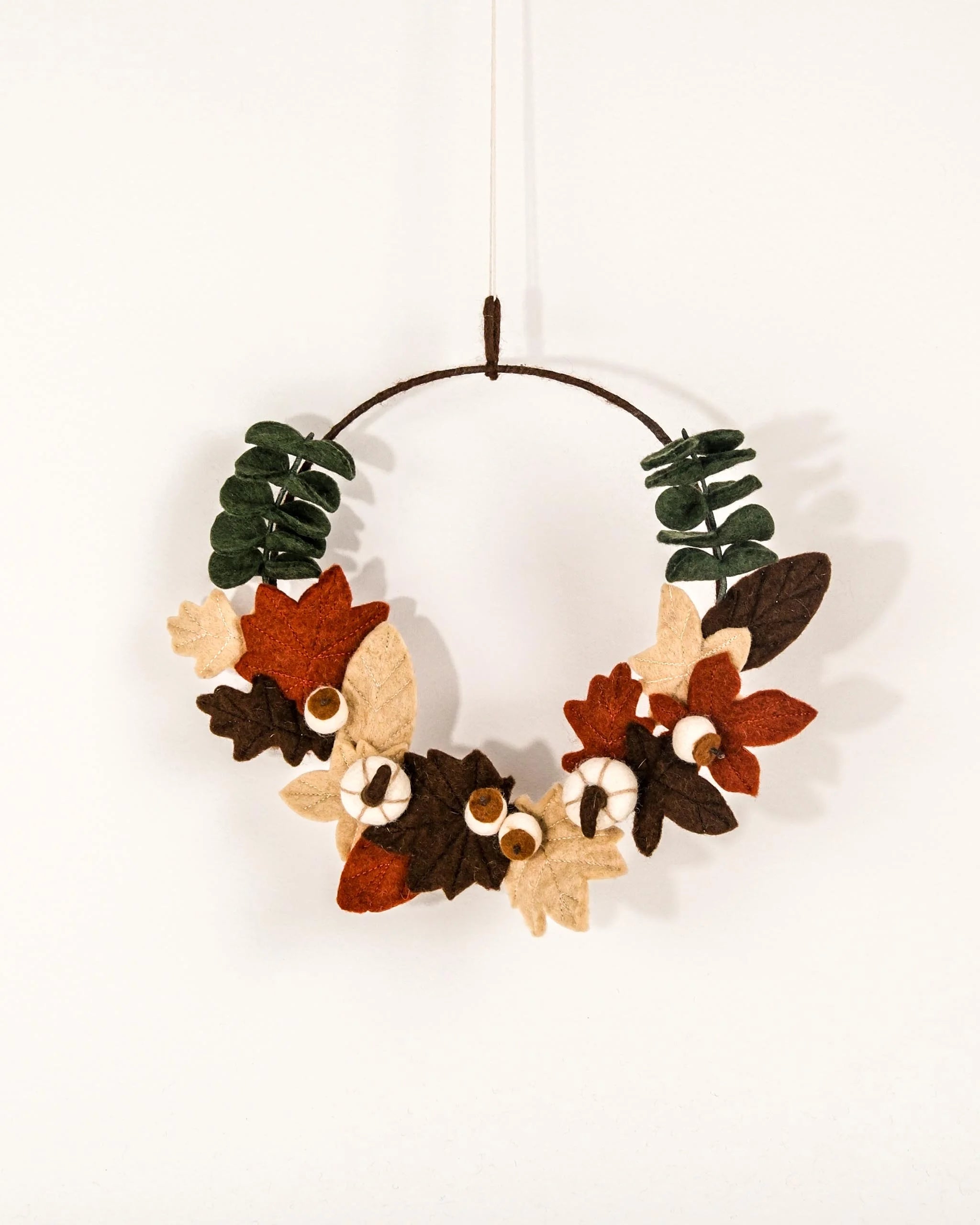 Couronne en feutrine citrouille sur un mur blanc.