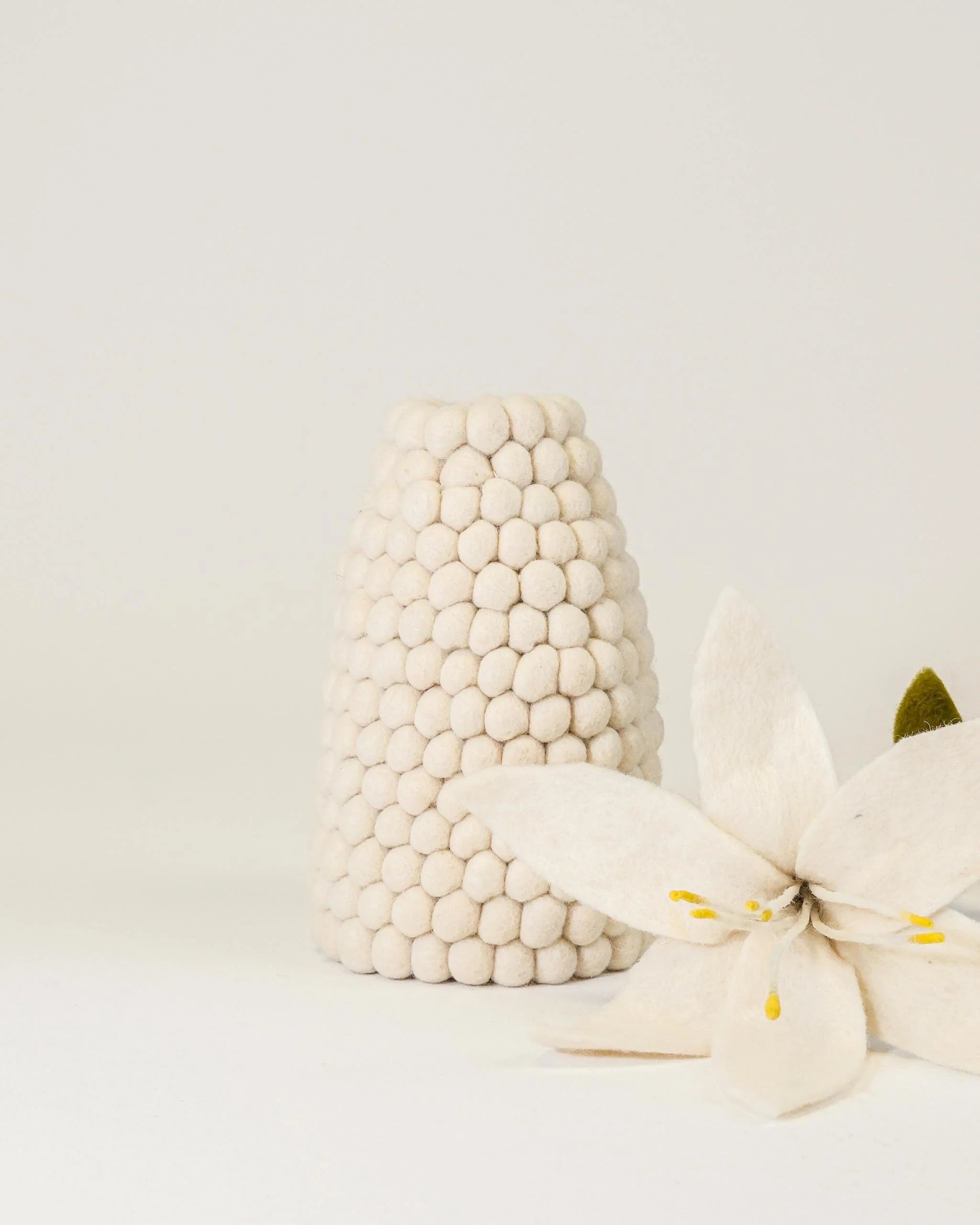Photo d'un vase en feutrine blanc sur un fond blanc avec une fleur de lys à coté. 