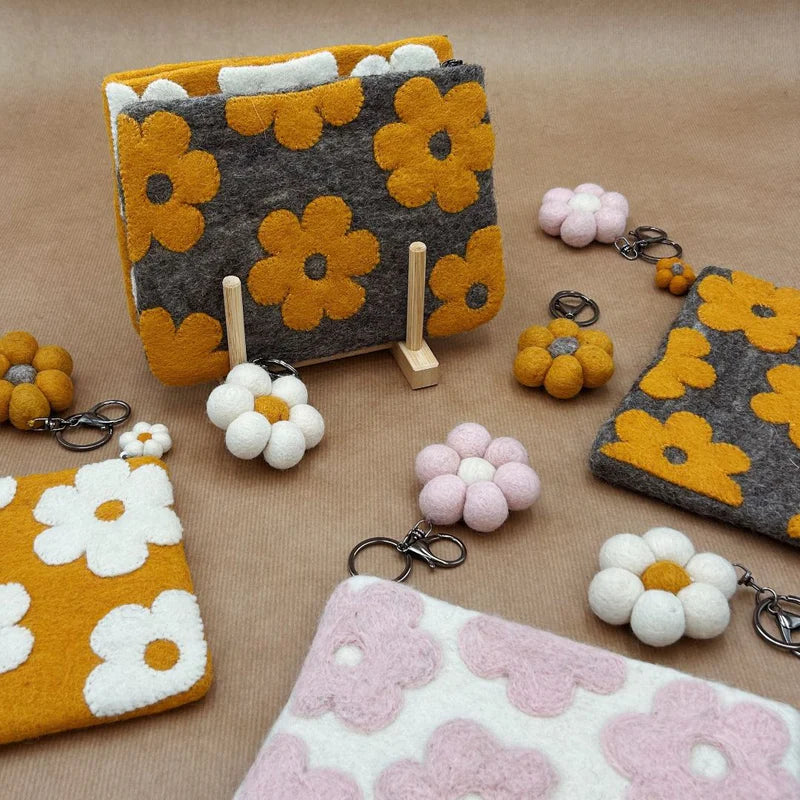 Assortiment de pochettes et porte-clés marguerites en laine feutrée, coloris jaune, marron et rose.