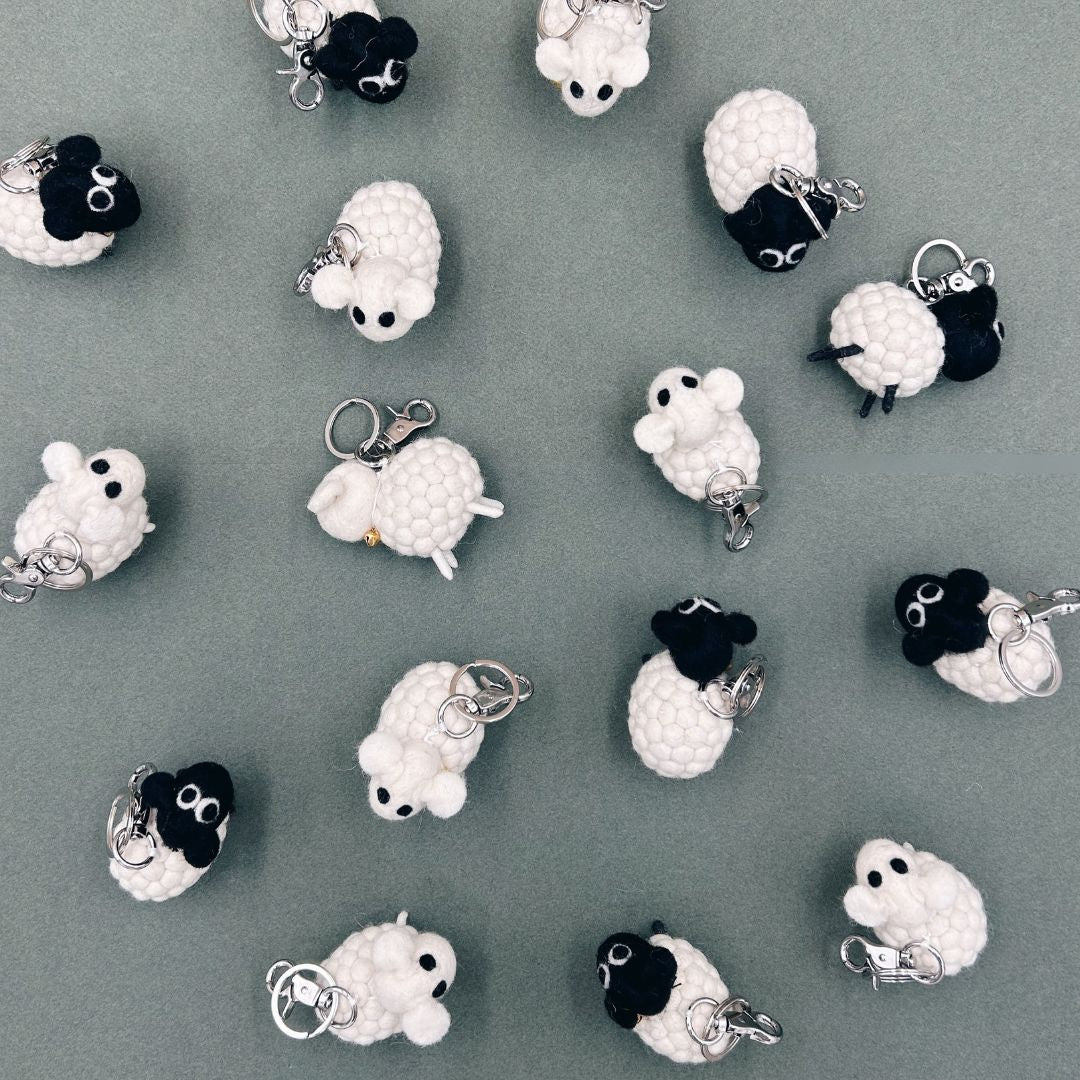 Accumulation de porte-clés moutons artisanaux en laine feutrée blanche et noire New Heidi vus du dessus.