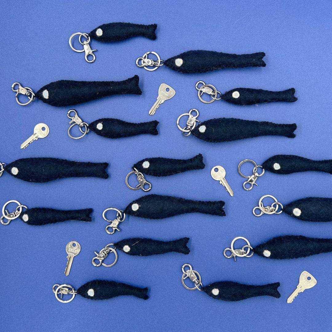 Banc de porte-clés poissons artisanaux en laine feutrée bleu marine New Heidi et petites clés posés sur un fond bleu.