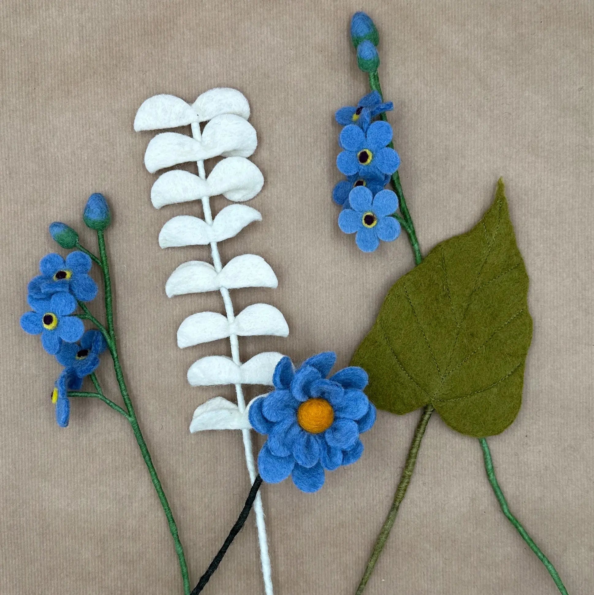 Présentation des tiges artisanales (anémone, myosotis, eucalyptus, feuille) du bouquet Azur Éternel.