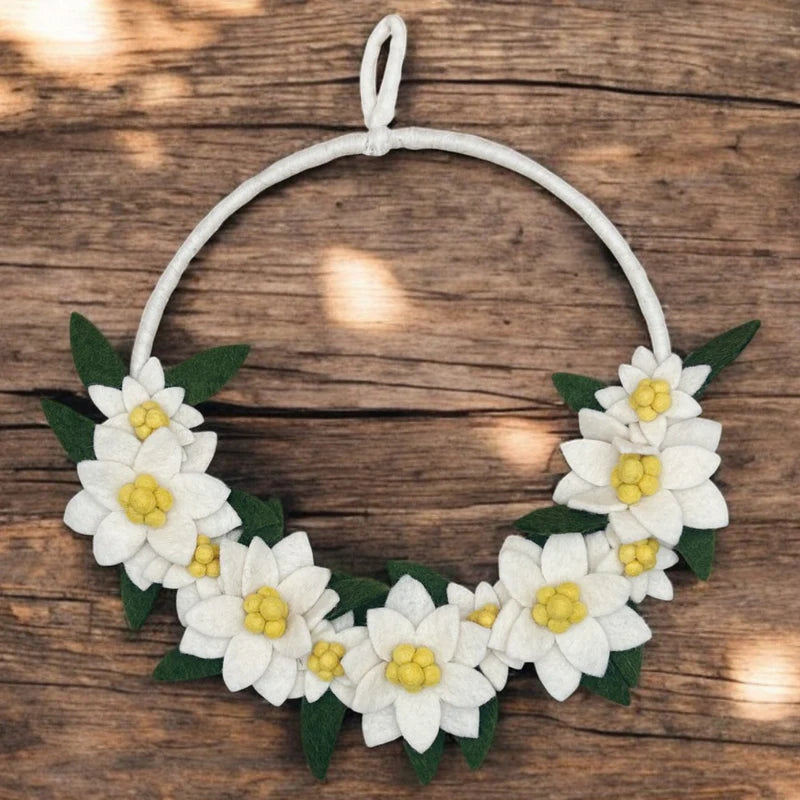 Couronne décorative d'edelweiss New Heidi en laine feutrée posée sur un fond en bois rustique.