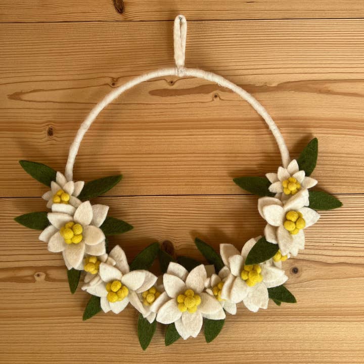 Couronne d'edelweiss New Heidi suspendue sur un mur sombre pour une ambiance chalet chic.