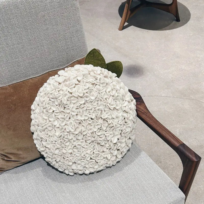 Coussin sculptural Hortensia New Heidi en feutrine blanche posé sur un fauteuil moderne.