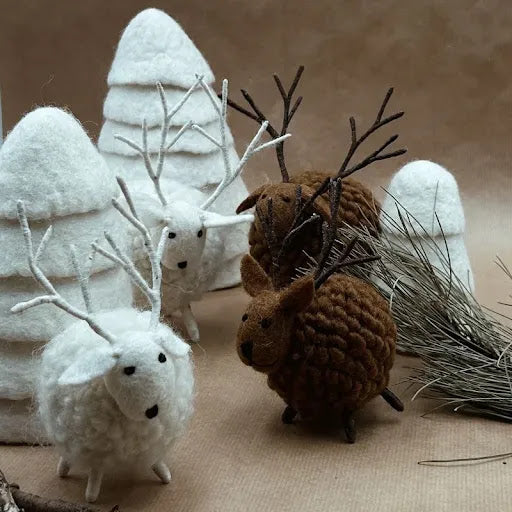 Mise en scène de cerfs en feutrine marron et blanc New Heidi avec des sapins artisanaux en laine blanche.