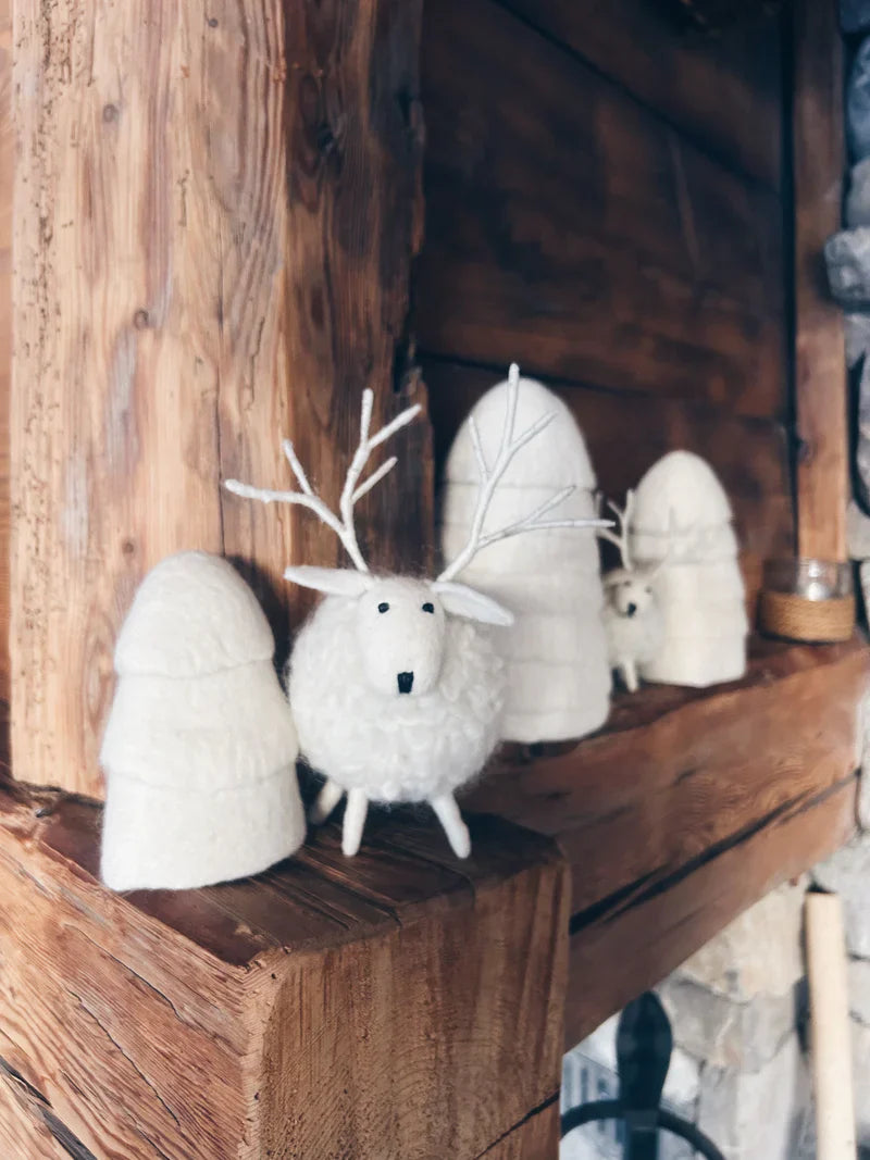 Mise en scène élégante d'un grand cerf blanc New Heidi sur un manteau de cheminée en bois avec des sapins en laine.