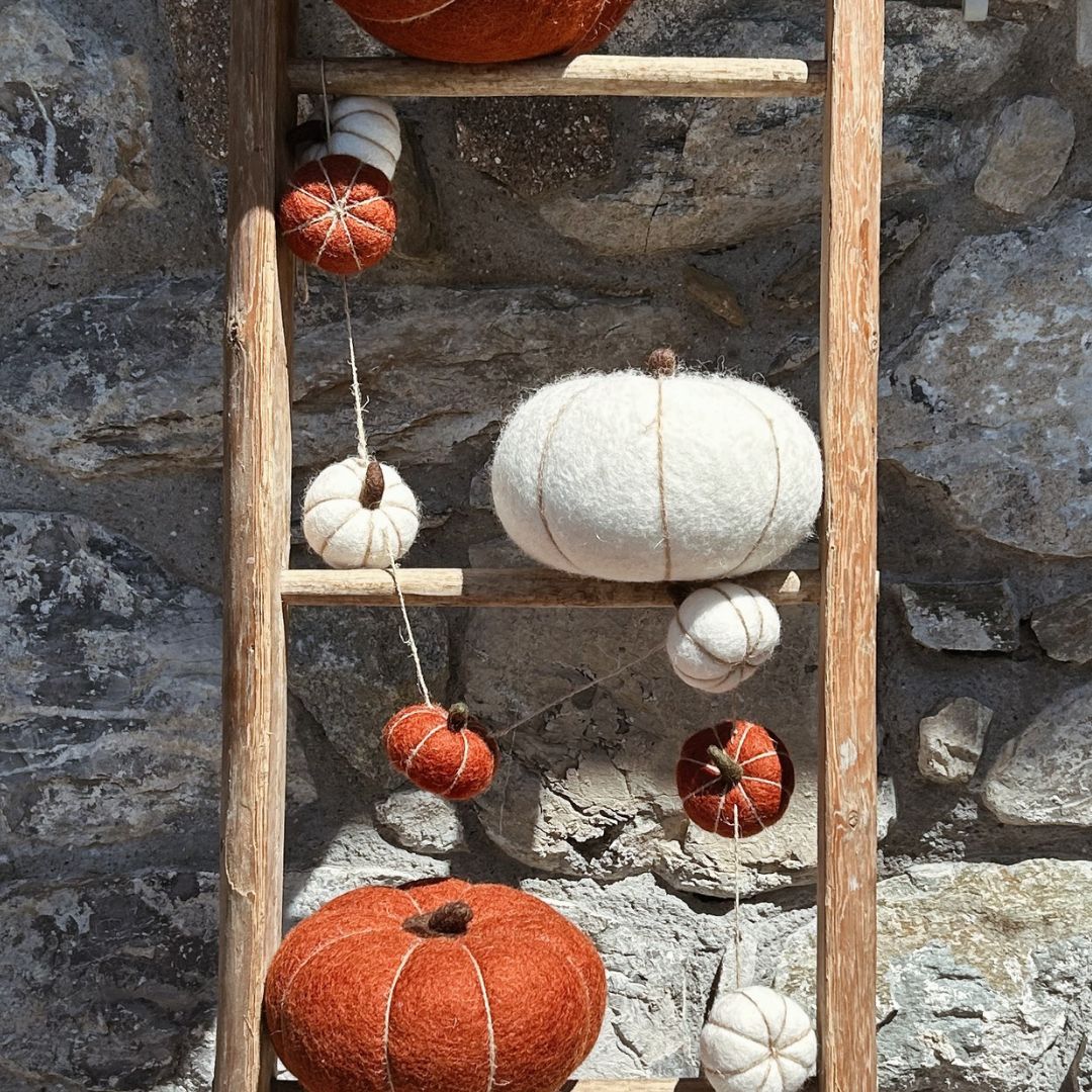 Guirlande de citrouilles en laine feutrée suspendue sur le manteau d'une cheminée avec une décoration d'automne style chalet.