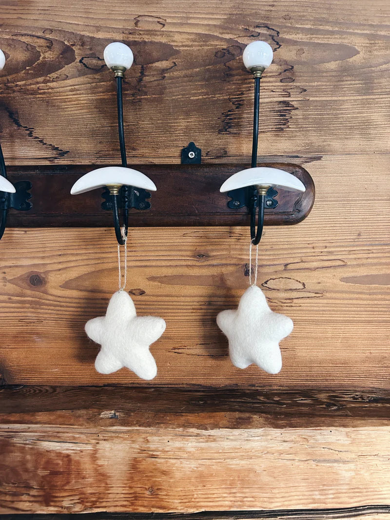 Deux étoiles en feutrine New Heidi suspendues à un porte-manteau rustique pour une décoration montagne chic.