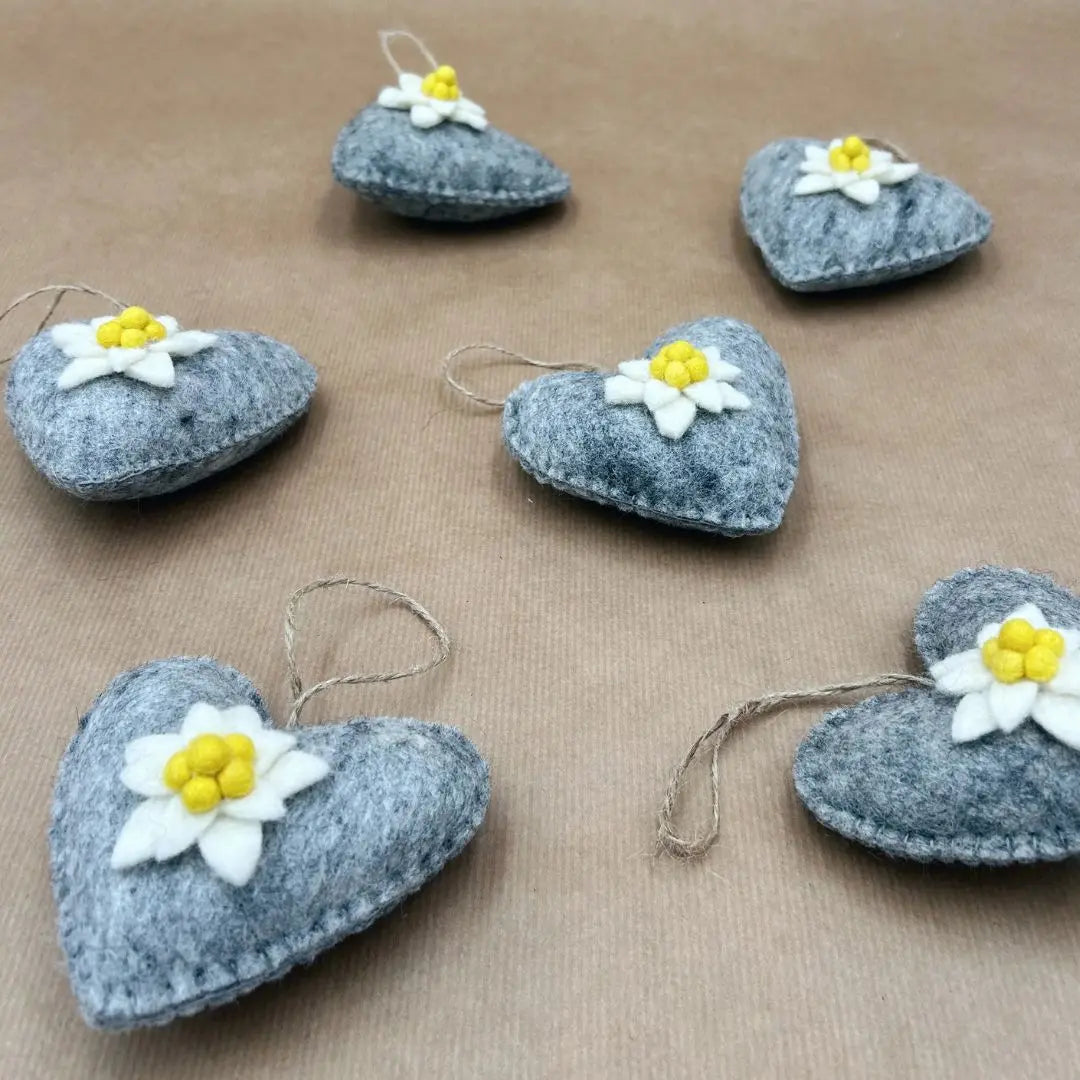 Composition de six cœurs en laine feutrée grise ornés d'edelweiss pour une décoration murale de montagne.