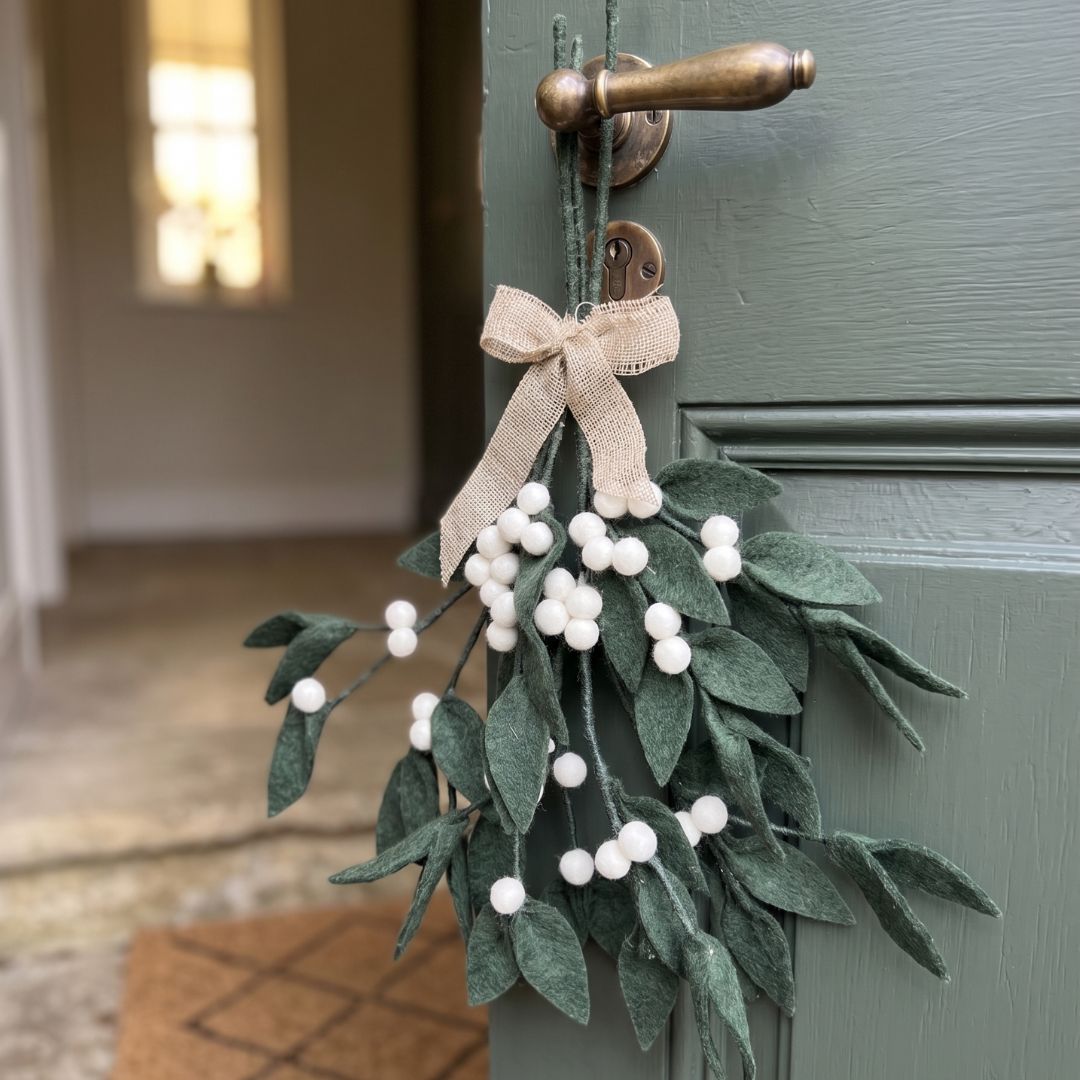 Bouquet festif de Noël composé de branches de gui en laine feutrée disposé dans un vase pour une décoration de table style chalet.