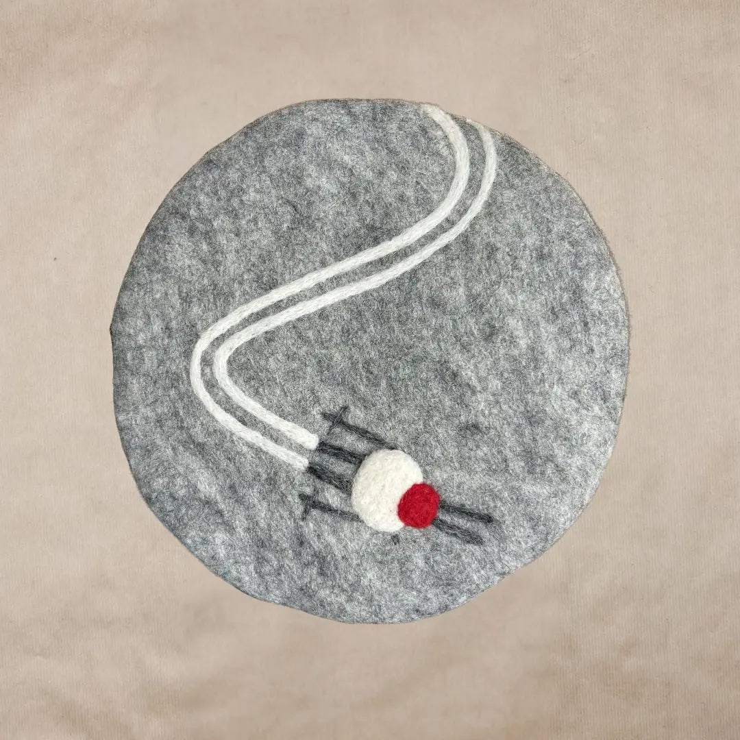 Dessous de plat rond en feutrine grise avec motif de trace de ski et skis brodés artisanalement par New Heidi.