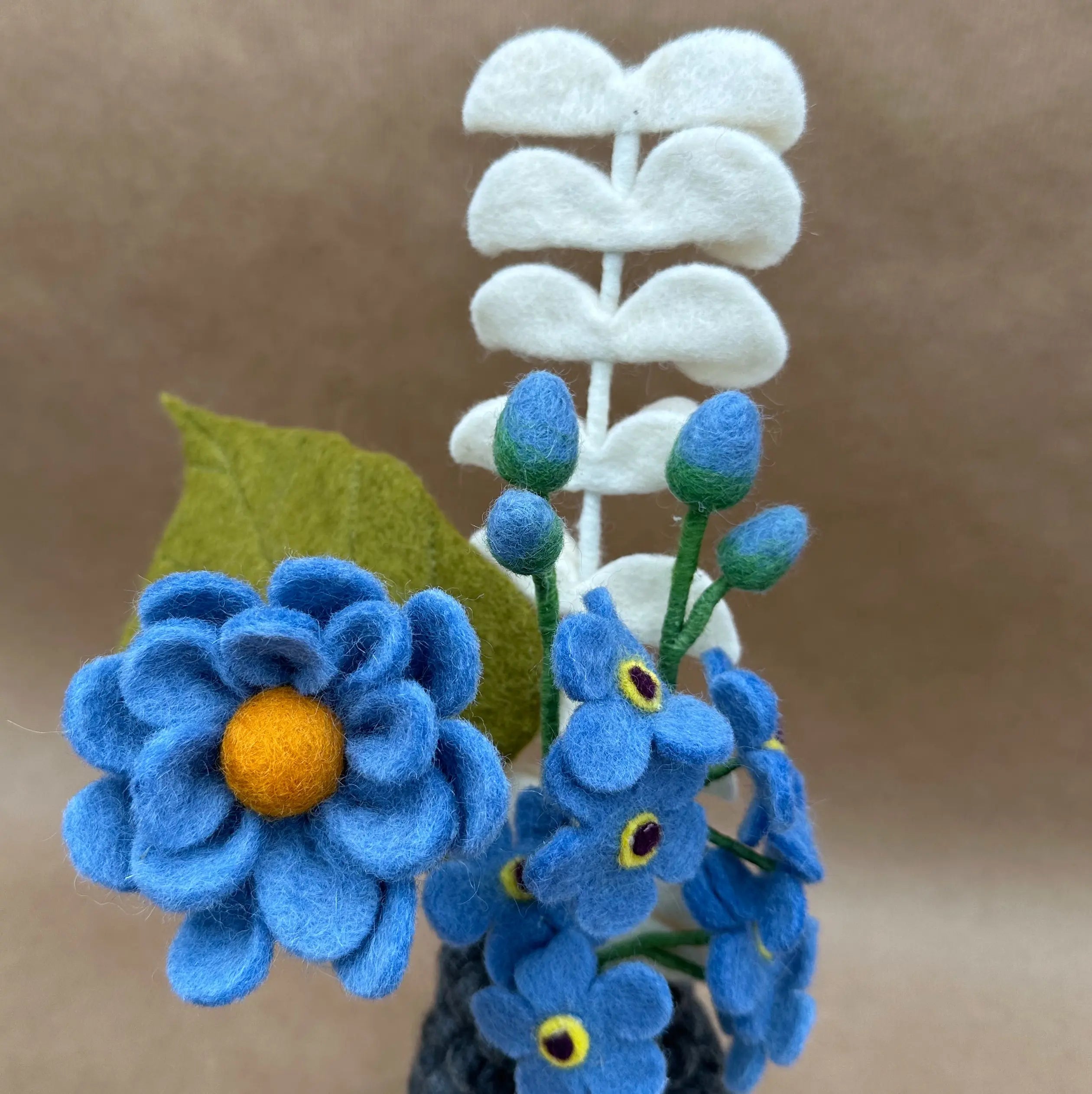 Gros plan sur les détails artisanaux de l'anémone bleu et des myosotis en laine New Heidi.