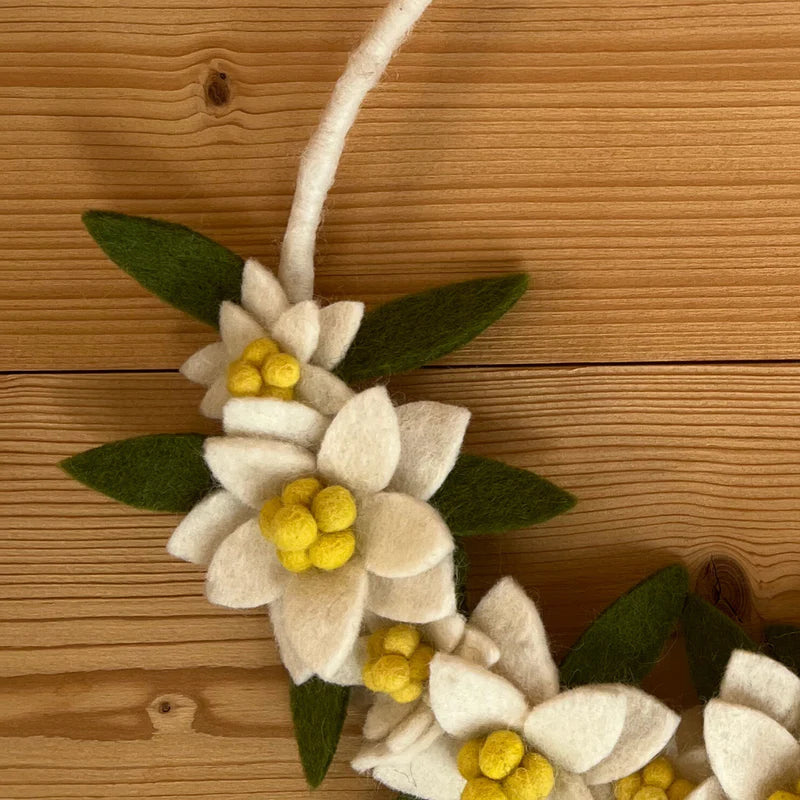 Détail des fleurs d'edelweiss faites main en feutrine blanche avec coeurs jaunes et feuilles vertes.