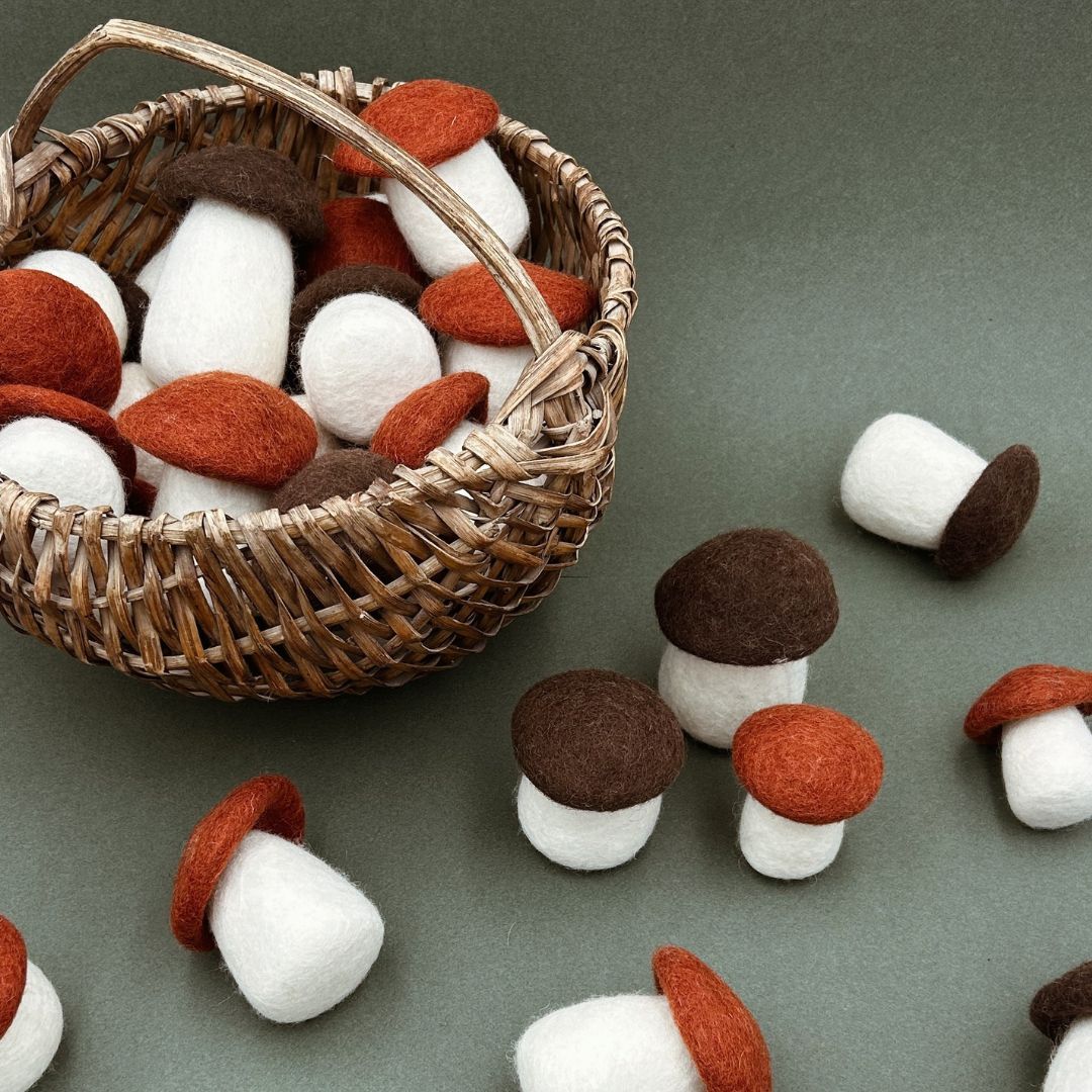 Panier en osier rempli de grands champignons bolets marron et orange en feutrine pour décoration automnale.