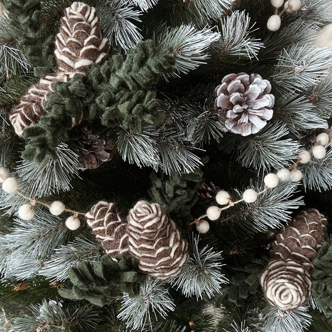 Décoration de Noël écoresponsable avec une pomme de pin en feutrine marron New Heidi suspendue à une branche de sapin.