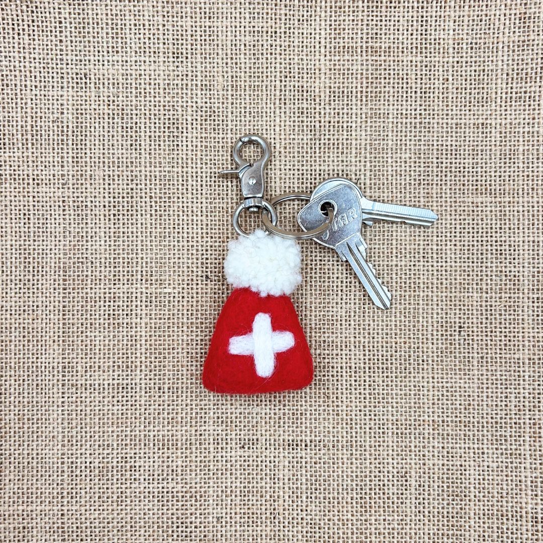 Porte-clé en feutrine rouge New Heidi en forme de bonnet drapeau Suisse avec croix blanche et pompon accroché à des clés.