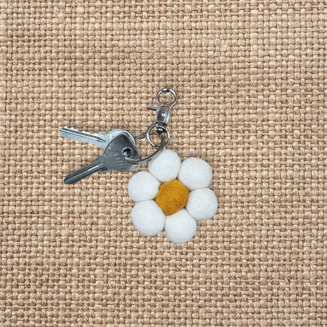 Porte-clé en feutrine en forme de marguerite blanche avec son trousseau de clés sur un fond en jute texturé.
