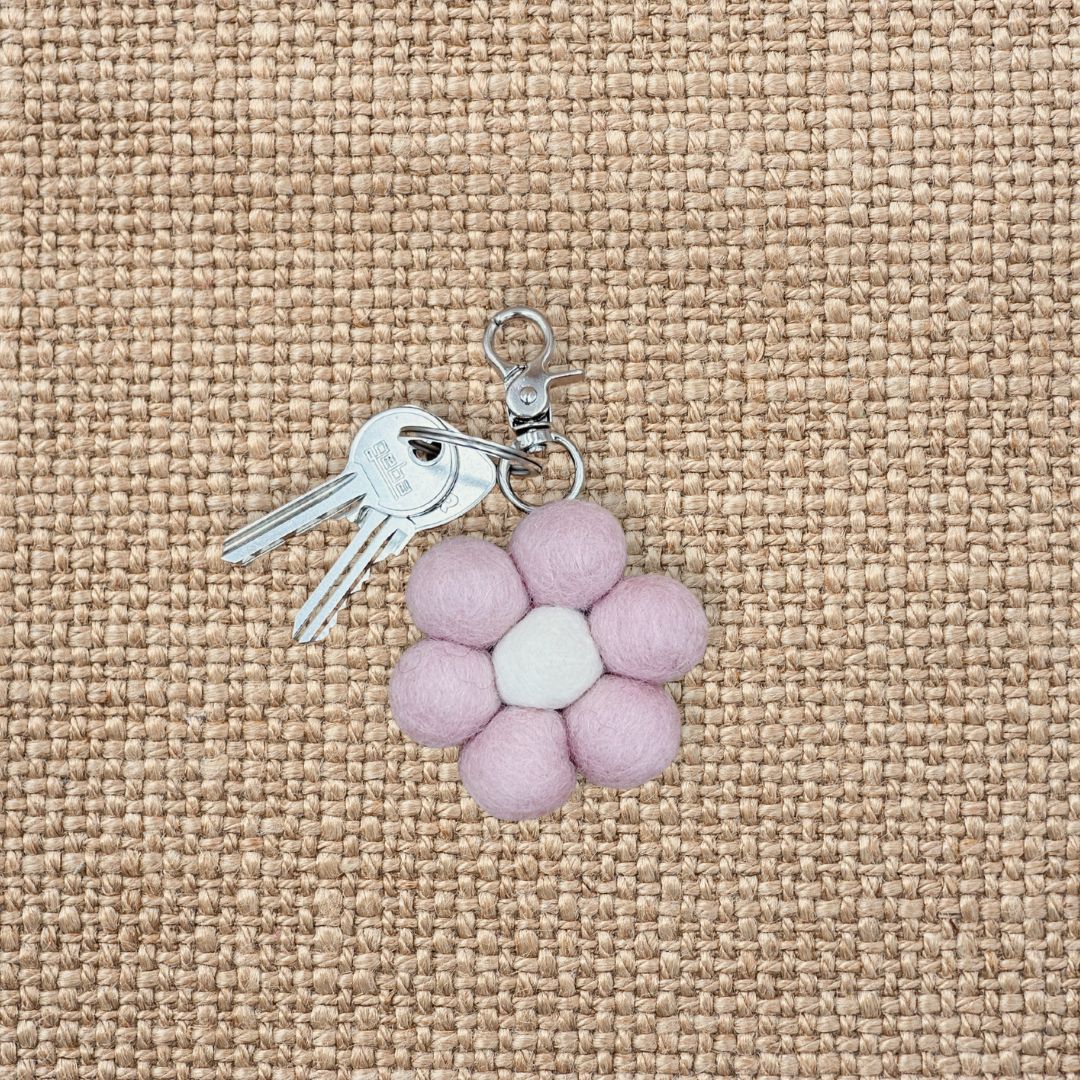 Porte-clé en feutrine en forme de fleur rose poudré avec son trousseau de clés sur un fond en jute texturé.