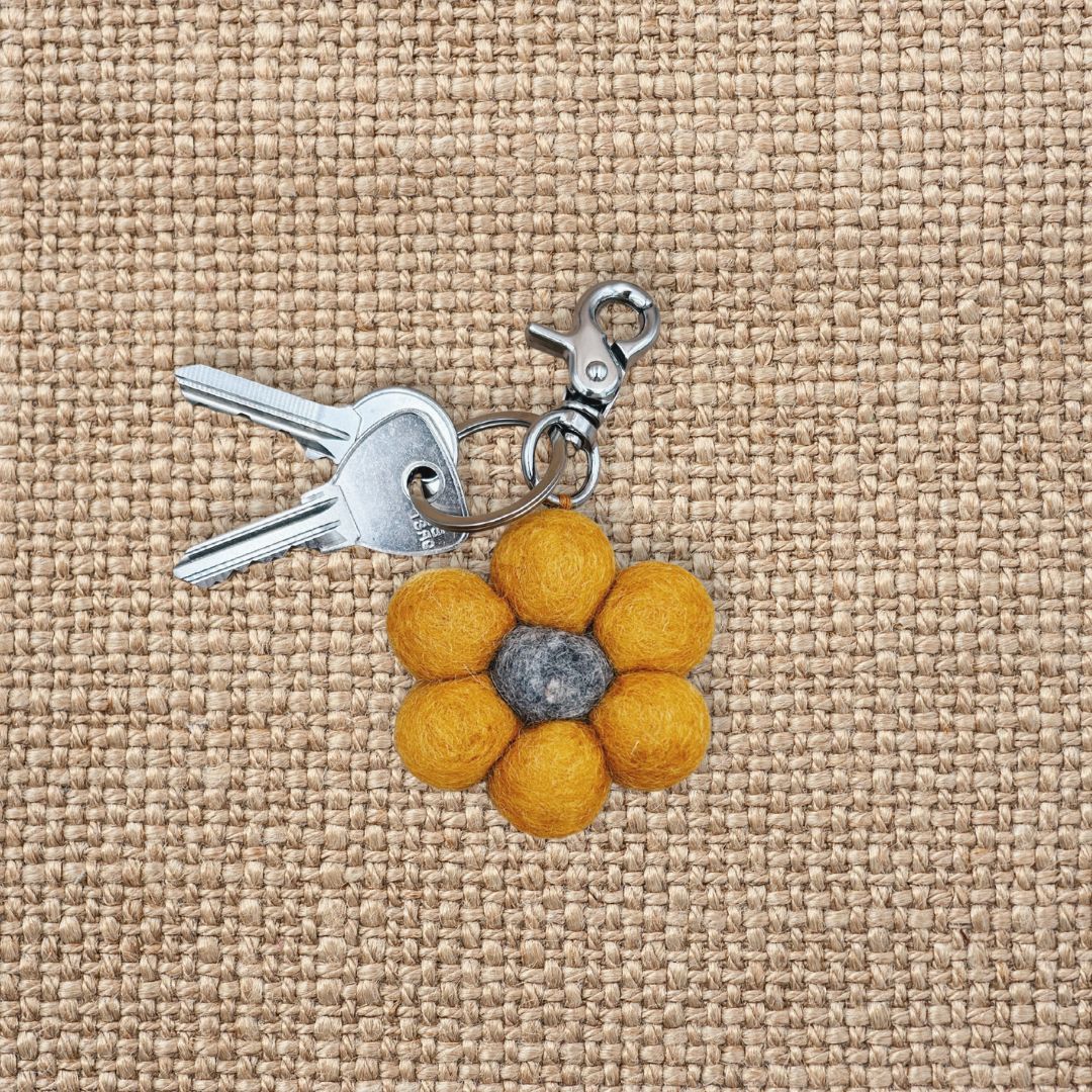 Porte-clé en feutrine en forme de tournesol jaune avec son trousseau de clés sur un fond en jute texturé.