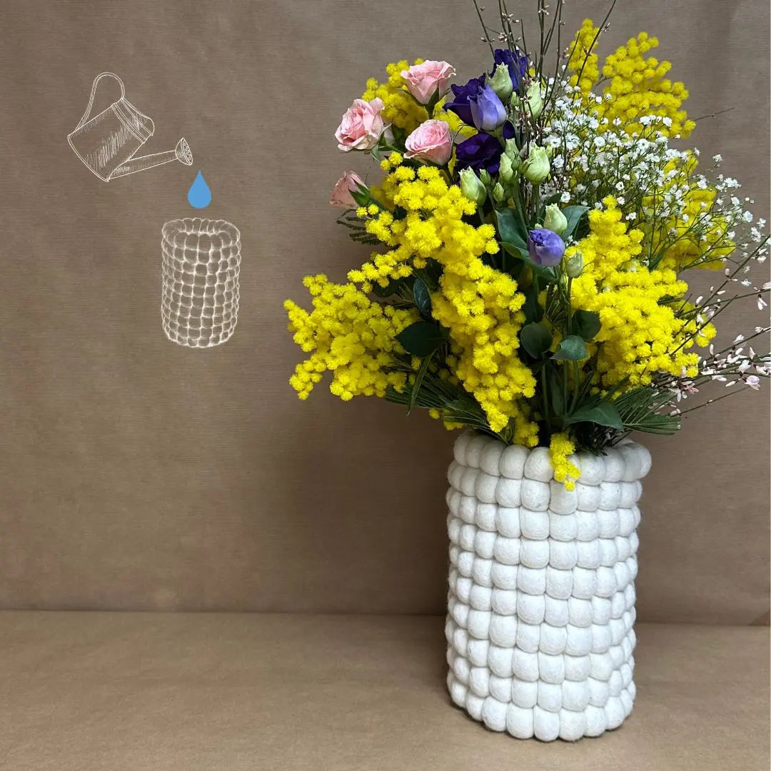 Vase en boules de feutrine blanche New Heidi accueillant un grand bouquet de fleurs fraîches et de mimosas.